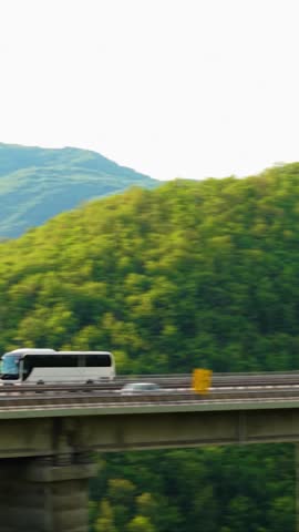 Passenger Bus Driving Along Mountain Road Surrounded by Lush Green Hills Aerial View