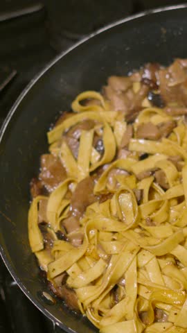 Vertical Overhead Video of Fresh Mushroom Tagliatelle Simmering in Hot Pan with Various Fungi Including Champignon, Shitake, Nameko. Home Cooked Cream Sauce Based Pasta Dish.