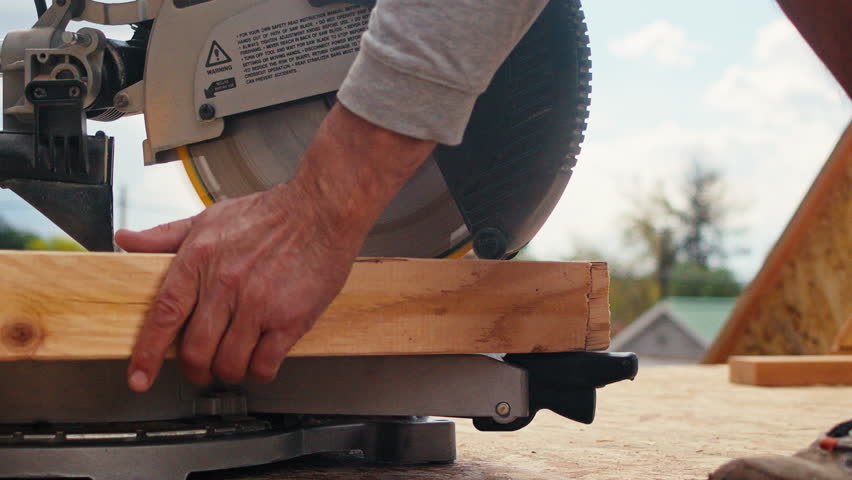 A carpenter working on a construction project uses a fast spinning chop saw to cut a line into a board.