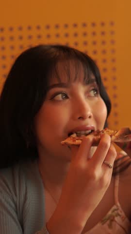 Attractive young Asian woman is enjoying and eating pizza for lunch in a restaurant or cafe.