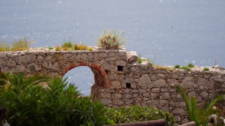 Stunning stone bridge in castle formation surrounded by nature with windy ocean in background in Taormina, Sicily, Italy (Italia)