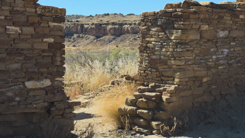 Stone doorway ruins leading to open canyon landscape under bright sky at Chaco Canyon, New Mexico.