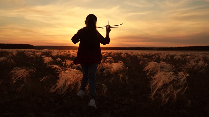Child girl aviator dreams of fly becoming pilot. Happy kid girl runs with toy airplane on field in sunset sky. Child play toy airplane. Little girl child wants to become pilot astronaut. Slow motion
