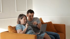 Man assisting pregnant woman using laptop, sitting together on comfortable sofa in cozy living room - Powered by Shutterstock - Get 15% off with code: PIKWIZARD15