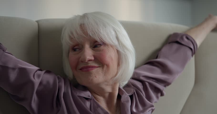 White haired lady woman in purple pajamas stretching and doing exercises after waking up in the morning. Mature woman stretching in the morning