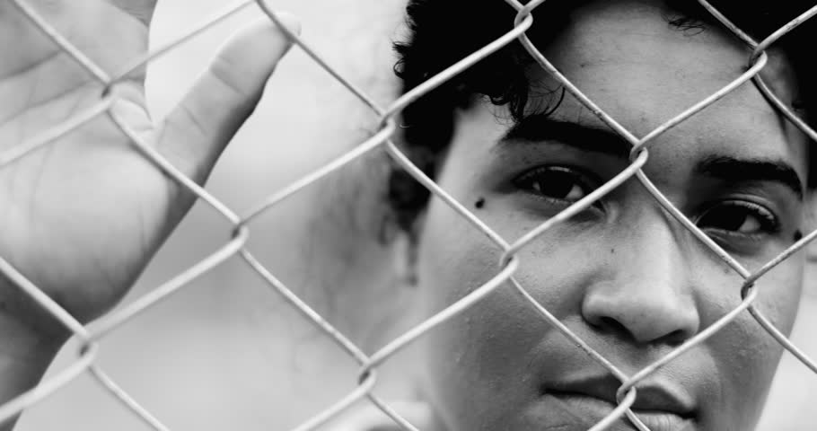 One Confined young black woman leaning on metal fence closing and opening eyes while hand holds on barrier tightly struggling in silence in dramatic monochrome, black and white