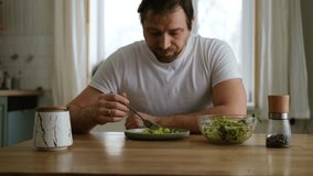 Handsome bearded man is eating green fresh vegan salad in the kitchen at home. Male sitting at table and eats vegetables, lettuce vegetarian meal. Happy athlete male enjoying Tasty healthy diet food. - Powered by Shutterstock - Get 15% off with code: PIKWIZARD15