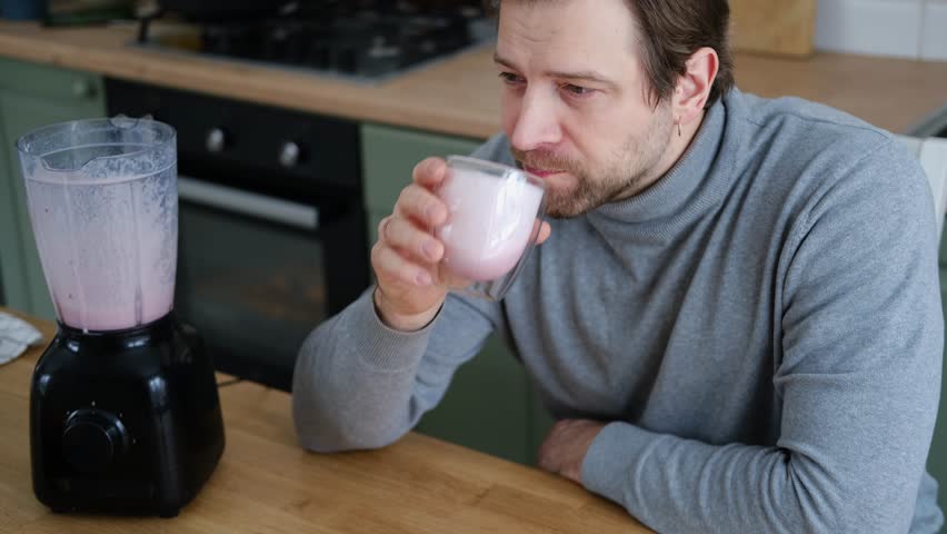 Handsome man making pink smoothie from fresh fruits in kitchen. Healthy food, health care nutrition. Bearded brutal athlete man drinking protein shake before training workout. Fitness dietary activity