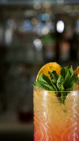 Close-up of a glass of Tequila Sunrise cocktail rotating on the bar counter. Vertical screen