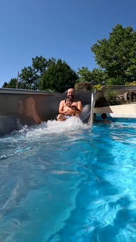 A man is riding a water slide with another person. The water is clear and calm. Scene is fun and playful