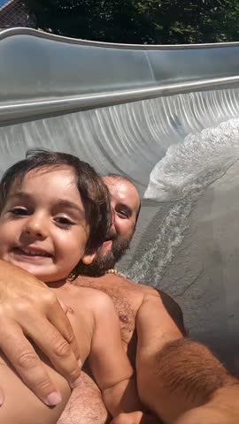A man and a child are sliding down a water slide. The man is holding the child's hand