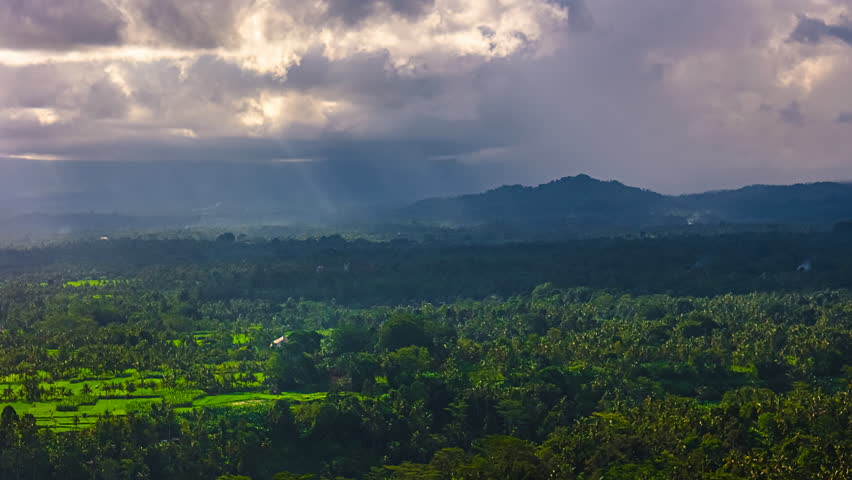 A dark cloud pack with some sunny openings drifts over a landscape in Bali, indonesia.