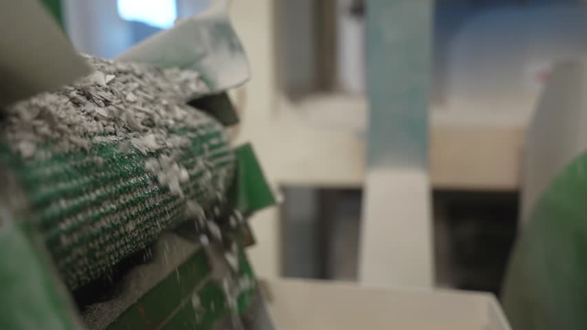Dry recycled material flow poured down from conveyor in manufacturing workshop. Processing reusable material for production with equipment closeup