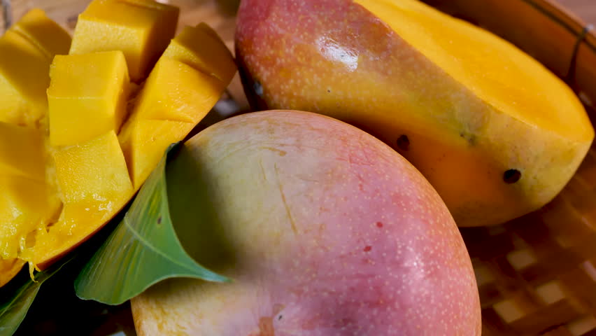 A ripe, juicy mango artfully presented on a woven bamboo tray. The mango is cut open, one half scored into neat, cube-like sections, slightly pushed outward to showcase the vibrant orange flesh.