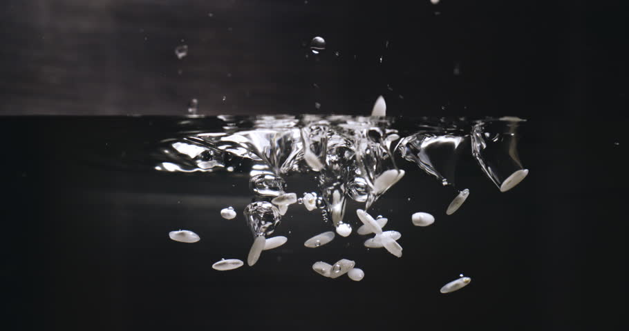 Super Slow Motion Macro of White Rice Dropping into Boiling Water. Grains Hit the Bubbling Surface in Stainless Steel Pot, High-Detail Food Preparation at 1000 fps.
