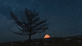 Orange tent on the slope near alone tree under moving Milky way at night - Powered by Shutterstock - Get 15% off with code: PIKWIZARD15