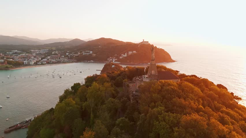 Aerial view of the beautiful coast of San Sebastian at sunset, Basque country, Spain. Flying over the statue of Christ stands watch over magnificent Bay of Biscay, Donostia. Orbit shot