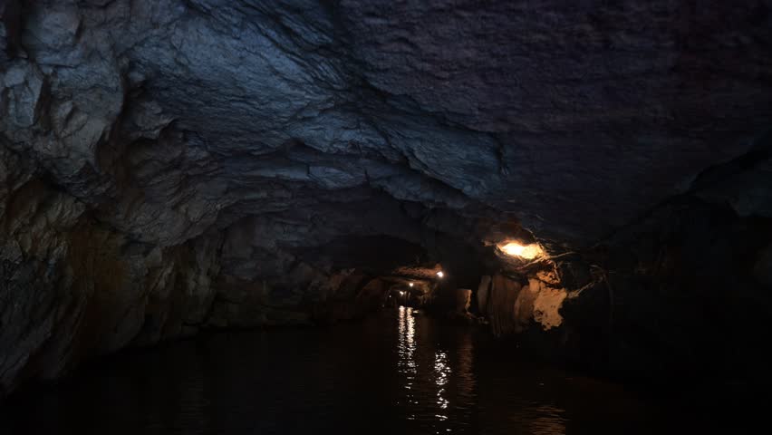 Travelers navigating cave waterways, gliding past dramatic rock formations and experiencing mysterious underground landscape with illuminating shadows