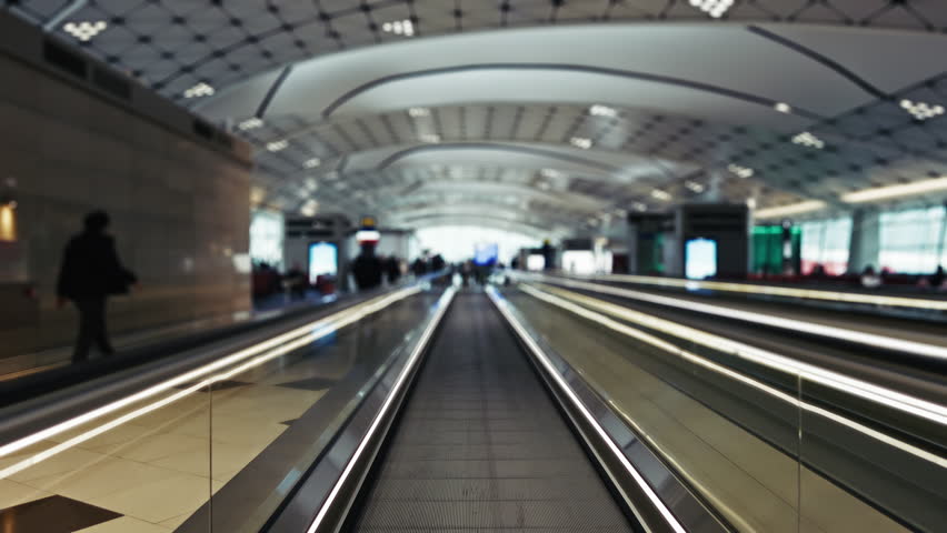 Moving walkway at Hong Kong Airport with blurred passengers and contemporary architecture. Brightly lit terminal showcases sleek design and bustling travel atmosphere