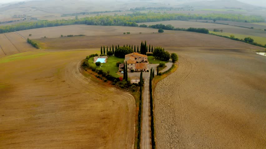 Drone over isolated Tuscan estate surrounded by farmland with long driveway and fields