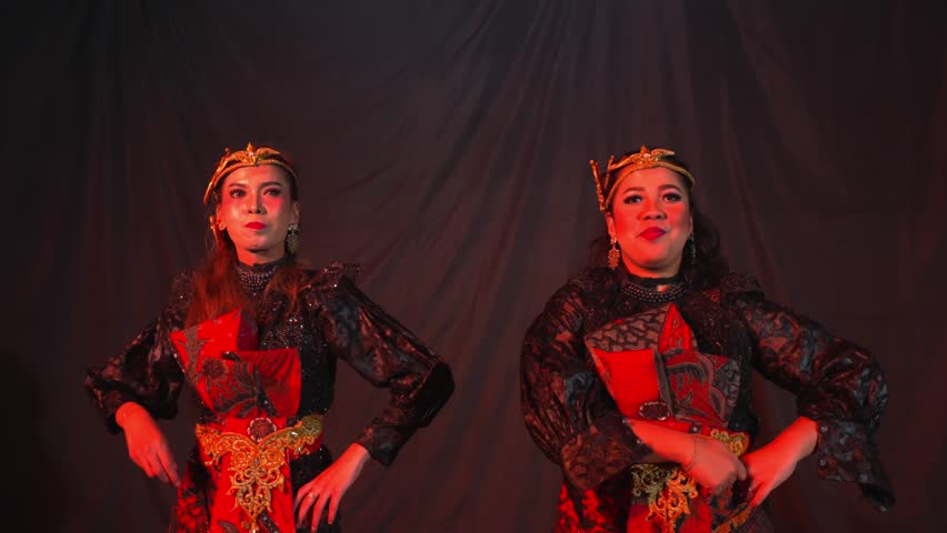 Two women in traditional attire performing a cultural dance with expressive movements and vibrant costumes.