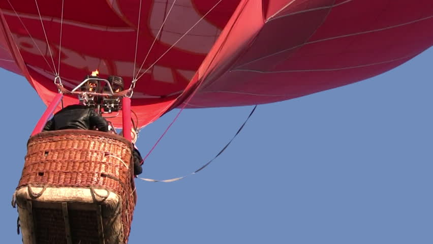 Red hot air balloon rises slowly in the air. In a gondola unrecognizable person