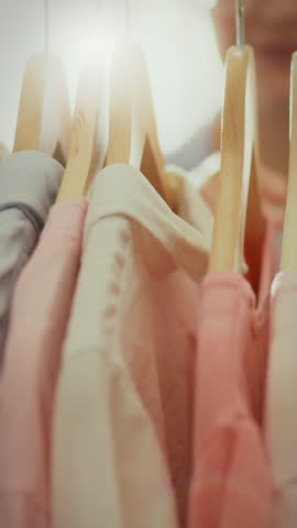 A young woman is carefully browsing through her home wardrobe, selecting outfits that reflect the latest fashion trends