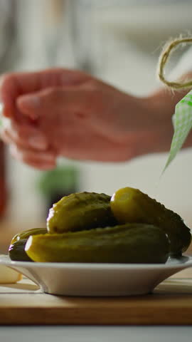 A woman is focused on making cucumber pickles in her home kitchen. She carefully selects cucumbers while preserving traditional methods, highlighting the joy of homemade food
