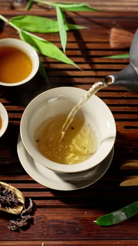 Pouring hot tea into tea cup on table.