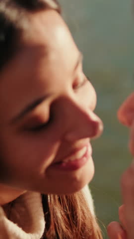 Vertical video, A young couple shares a tender kiss by the water. They hold each other close, savoring the moment and the warmth of their love.