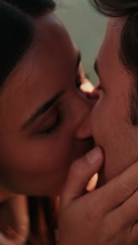 Vertical video, A young couple shares a tender kiss by the water. They hold each other close, savoring the moment and the warmth of their love.