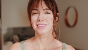 Happy woman smiling at the camera at home. She is wearing a green tank top and has auburn hair. Sunlight streams in from a nearby window. - Powered by Shutterstock - Get 15% off with code: PIKWIZARD15