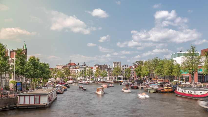 Boats floating and passing by near the National Opera music and theatre venue timelapse. Houseboats on the river in Amsterdam under a cloudy sky. Popular tourist destination in the Netherlands