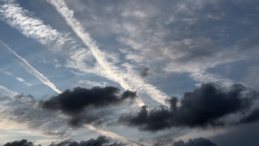 Evening clouds drift in realtime across a subtropical sky, with small dark clouds in contrast with long, bright, dissipating contrails. For motifs of bygones and transition, yin and yang, ephemera.