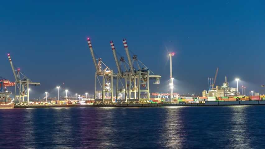Night timelapse of Hamburg cargo port, showcasing container terminals, cranes and cargo ships on the Elbe River. Boats and vessels pass by, creating a dynamic maritime panorama. Germany