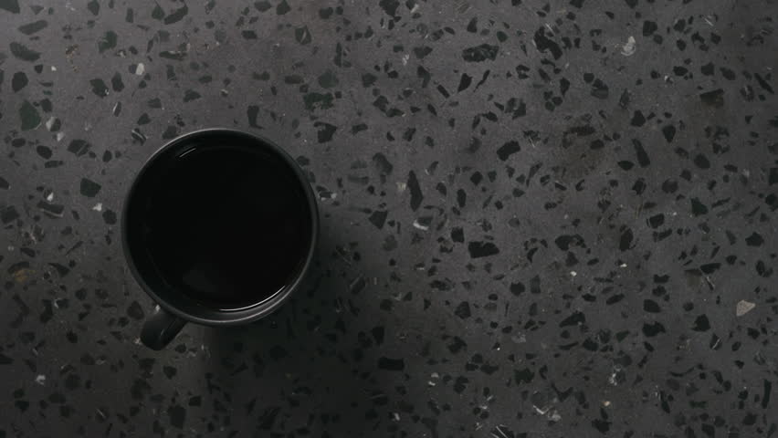 Slow motion pour cream into black coffee in black cup on concrete background top view