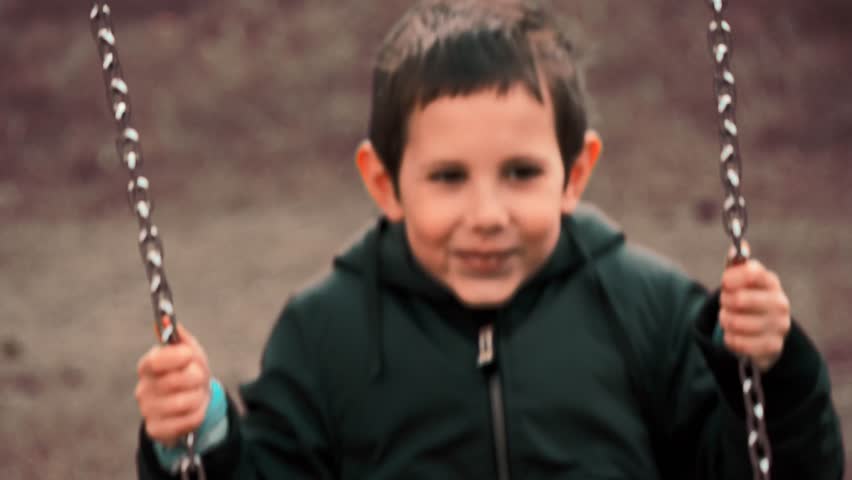 Happy Child on Swing in Autumn Park – Slow Motion, boy bathed in warm, golden light that evokes a sense of nostalgia and simpler times. The scene captures a classic childhood moment  
