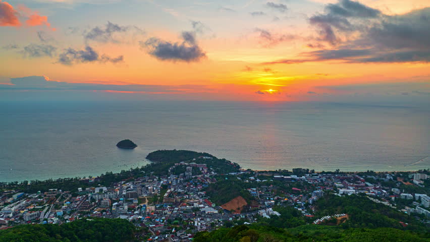 Aerial hyper lapse view of A breathtaking the iconic Big Buddha statue overlooking the Andaman Sea in Phuket, Thailand, captured during a vibrant sunset. The colorful sky reflects on the water.