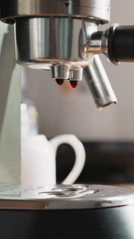 Beverage drops fall down on coffeemaker tray. Young woman holds ceramic cup of ready-made coffee near coffee machine. Comfort of morning routine