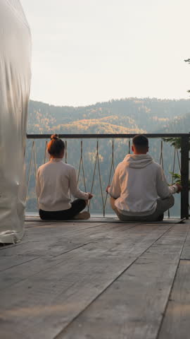 Couple meditates on glamping house terrace in morning. Young man and woman do mind clearance practices at eco resort. Finding inner peace in nature