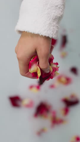 Lady pours flower petals into foamy water. Woman in soft bathrobe adds roses in hot water for bathing preparing relaxation procedure. Spa relaxation