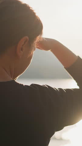 Lady covers face with hand looking ahead. Woman feels lonely sitting on riverbank with scenic view. Gathering thoughts with calm atmosphere of nature