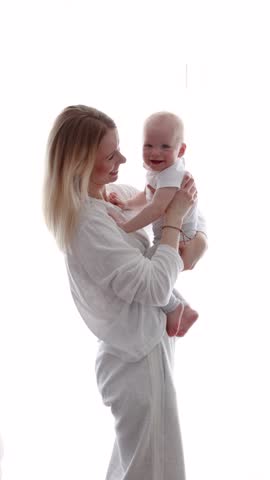 Mother and daughter. Happy smiling blonde mom hugging Little baby at home in front of white background with copy space, love, tenderness, motherhood and family connection