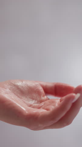 Female pours liquid product into hand to apply to hair in shower. Flowing moisturizing shampoo drips onto hand in bathroom with blurred background