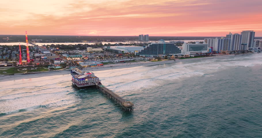 Coastal city of Daytona Beach, Florida with Main Street Pier and Breakers Oceanfront theme park with amusement swings, illuminated luxury hotels at sunset. Tourism infrastructure in southern USA.