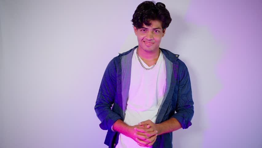 Male model smiles while posing under bright light, Trendy poser glows in studio flash setup, Casual Style Meets Magazine Perfection, Dynamic gaze captivates camera, Man stands posturing with bold look