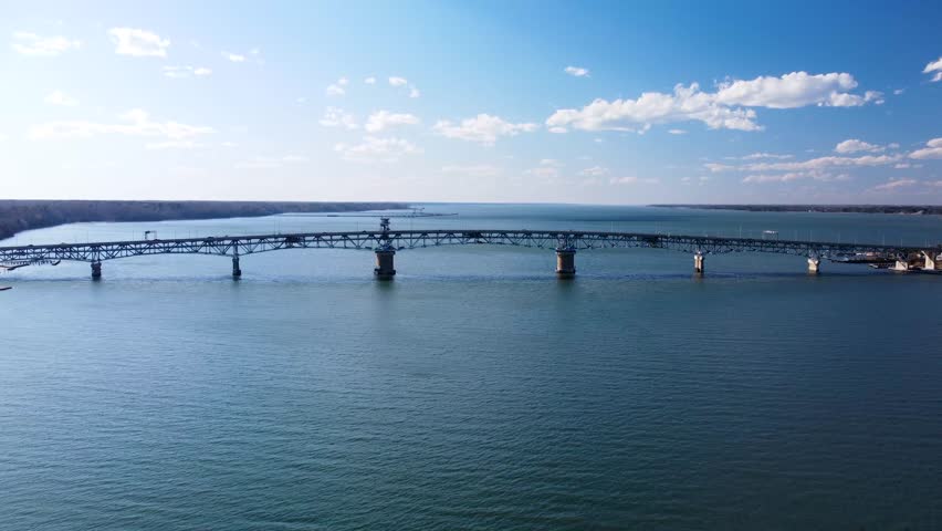 Aerial view of the Coleman Memorial Bridge stretching across the York River into Yorktown, Virginia, on a clear, sunny afternoon with light traffic and calm waters.