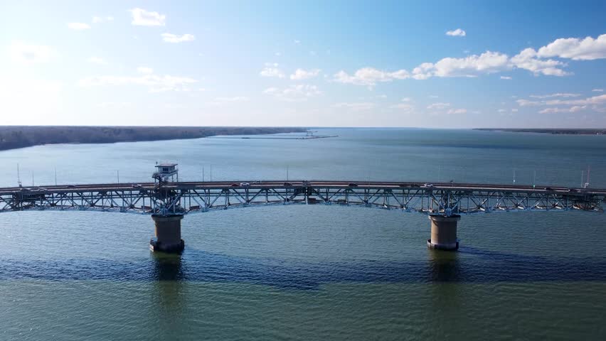 Aerial view of the Coleman Memorial Bridge stretching across the York River into Yorktown, Virginia, on a clear, sunny afternoon with light traffic and calm waters.