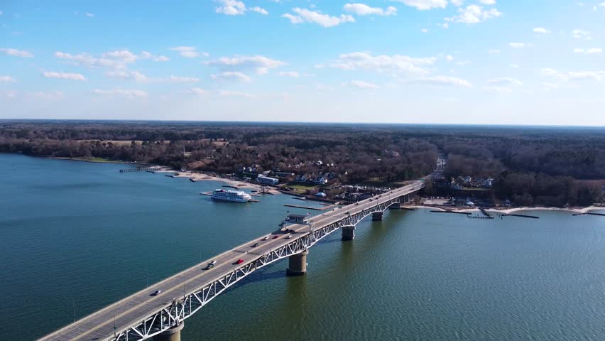 Aerial view of the Coleman Memorial Bridge stretching across the York River into Yorktown, Virginia, on a clear, sunny afternoon with light traffic and calm waters.