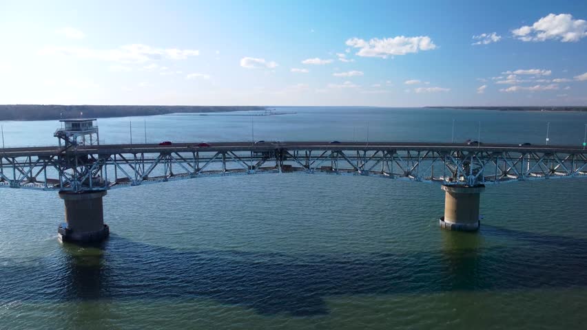 Aerial view of the Coleman Memorial Bridge stretching across the York River into Yorktown, Virginia, on a clear, sunny afternoon with light traffic and calm waters.